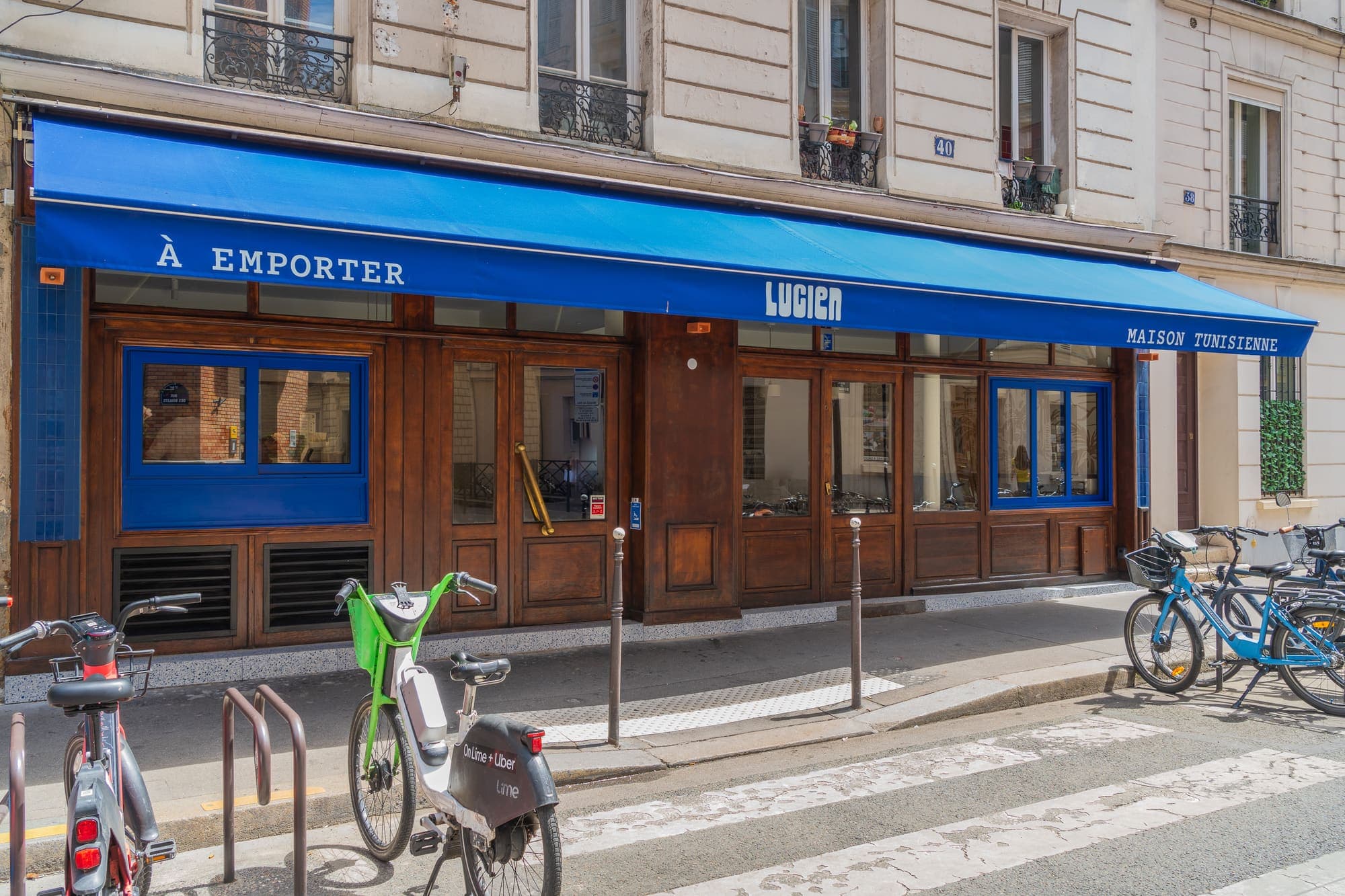 Façade du restaurant Lucien, store bleu « à emporter » et vélos garés devant.