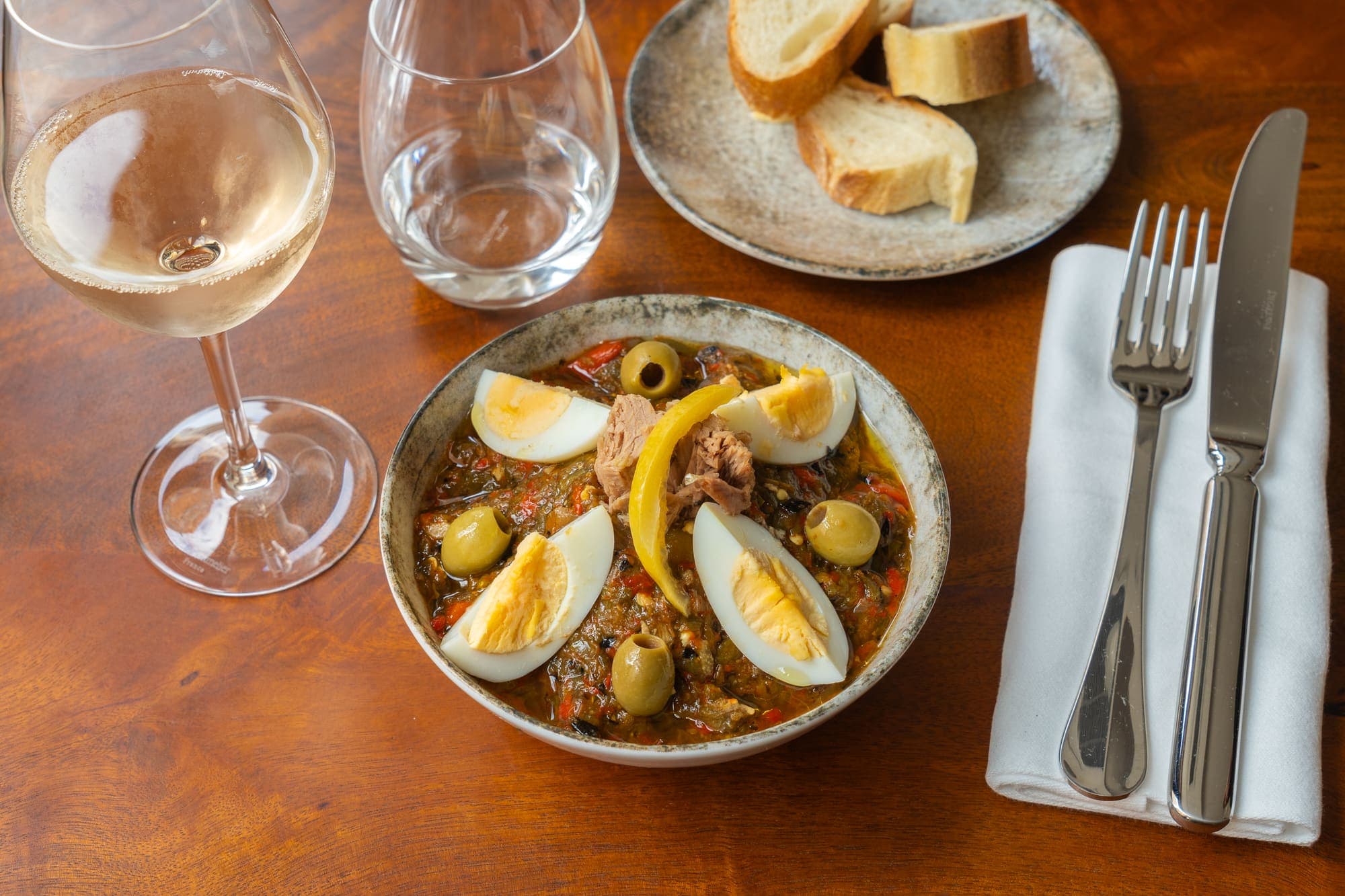 Slata mechouia servie avec œufs et thon, verre de vin blanc sur la table.