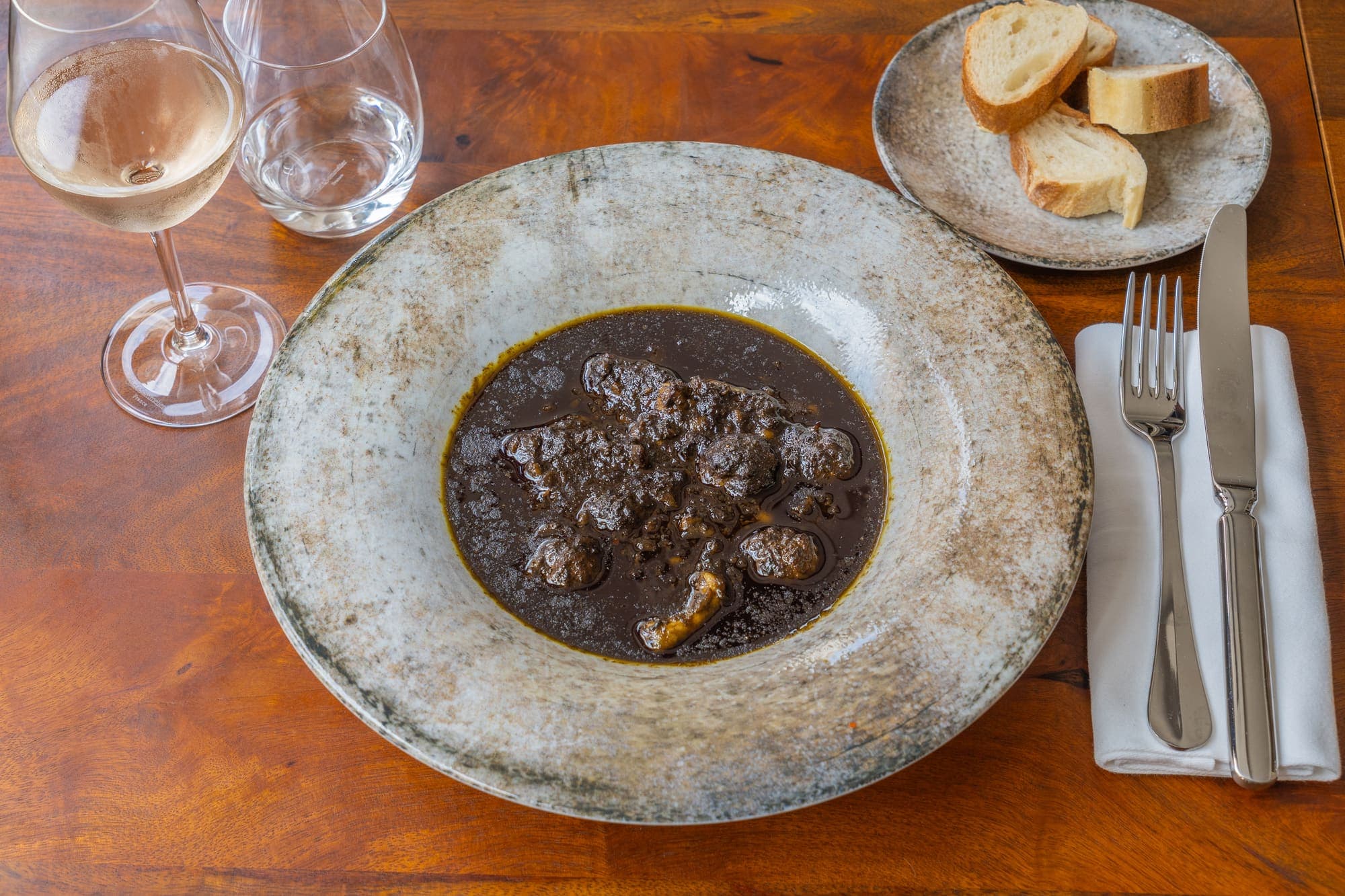Boulettes en sauce servies avec du pain, verre de vin sur une table en bois.