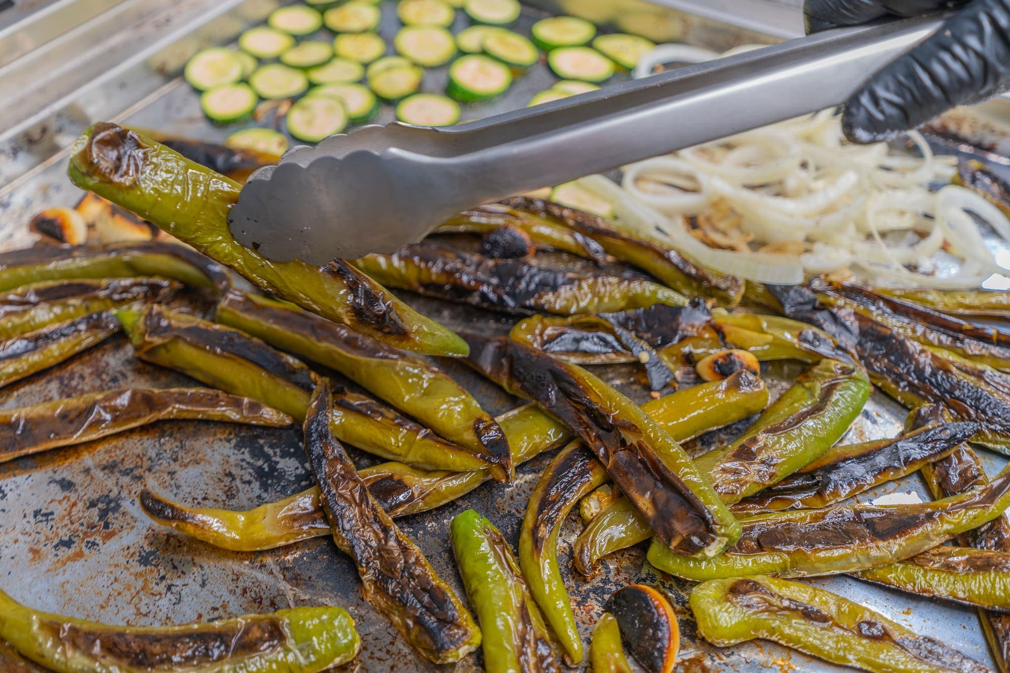 Poivrons et courgettes grillés sur la plancha, retournés à la pince.